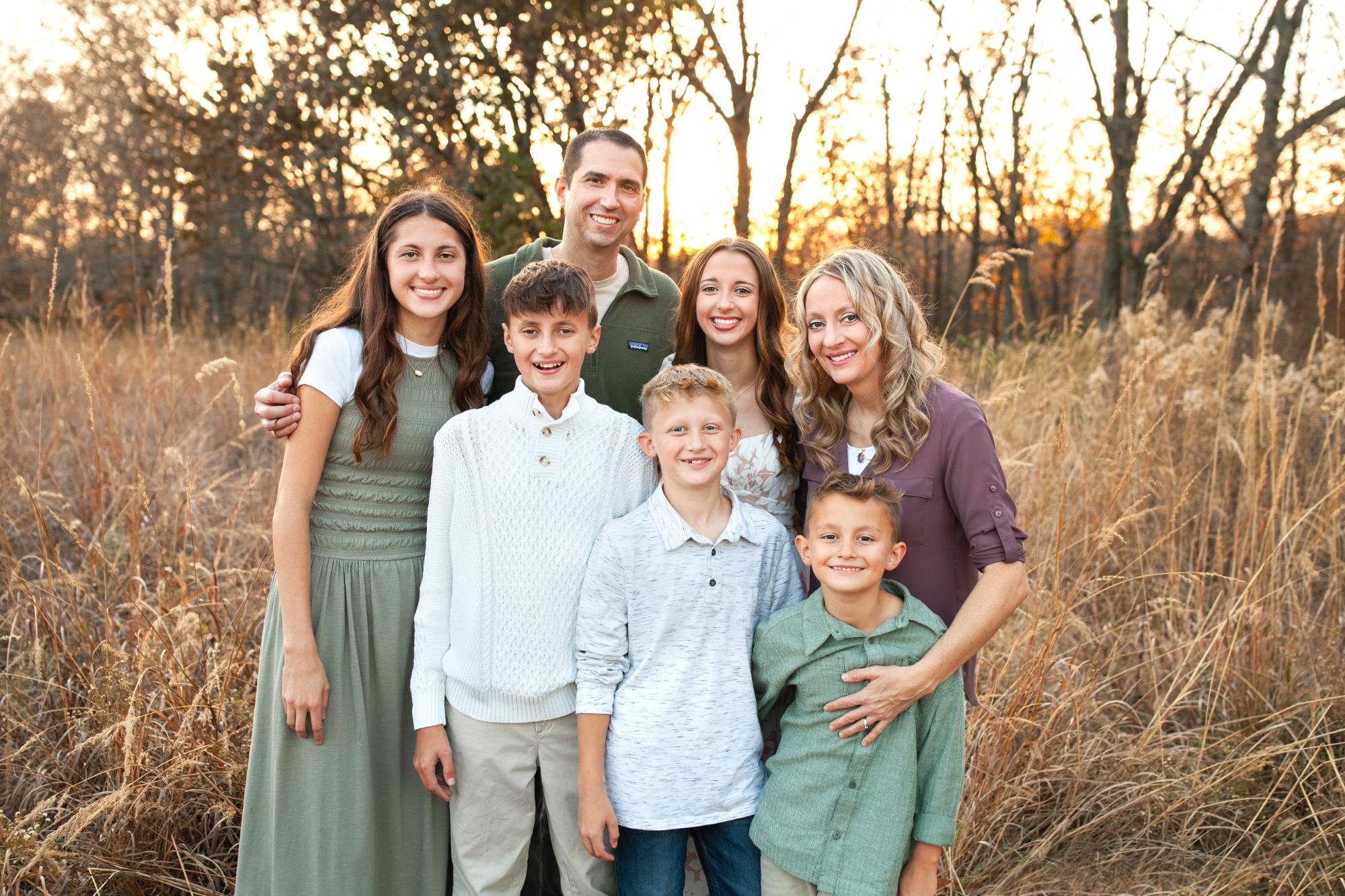 Dr. Walker page Family portrait of Dr. Cameron Walker with his wife Teresa and their five children, smiling in a natural outdoor setting during sunset, reflecting his commitment to family and personal life.