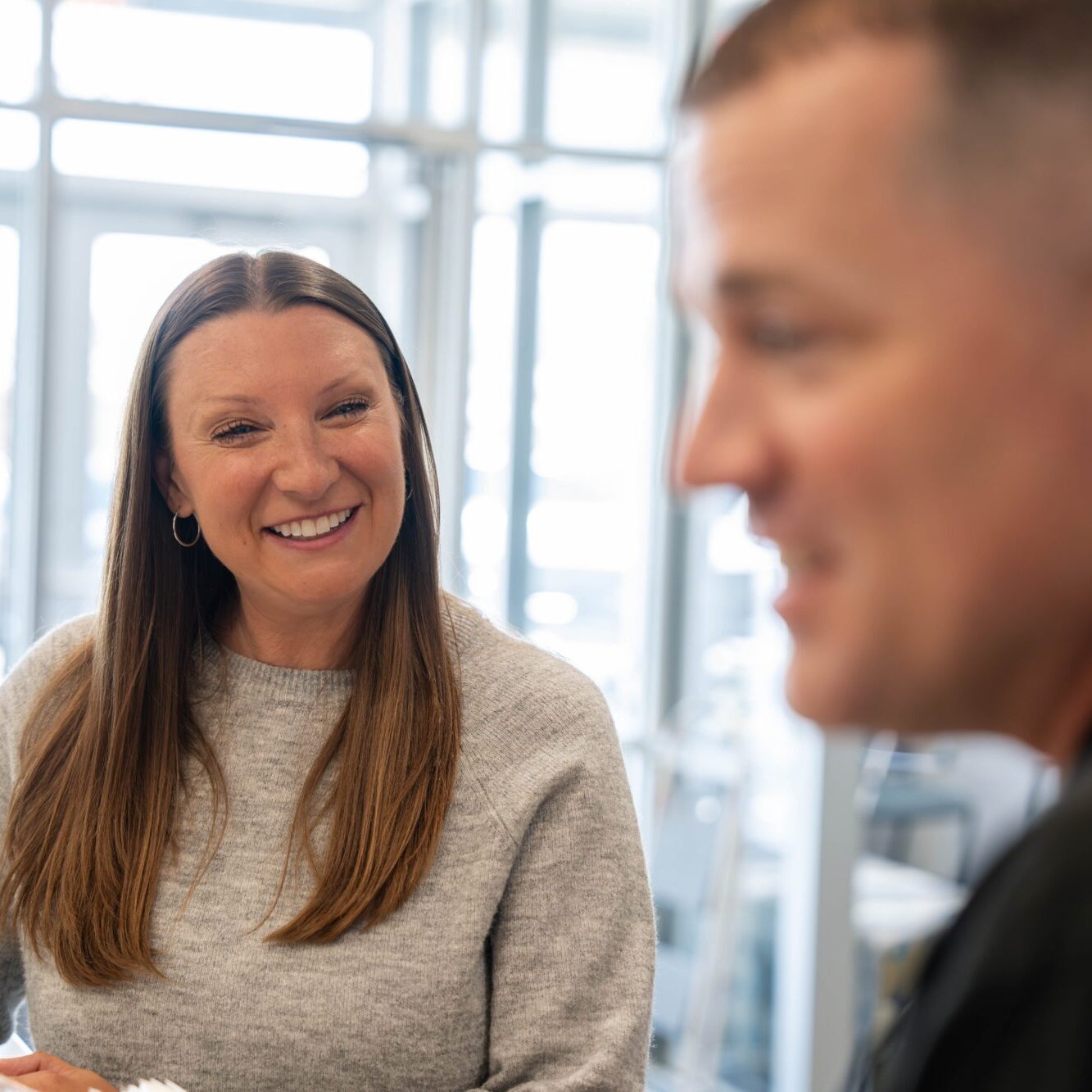 Smiling woman in casual sweater engaging with a man, showcasing a positive interaction in an orthodontic office setting, reflecting patient satisfaction and transformation.