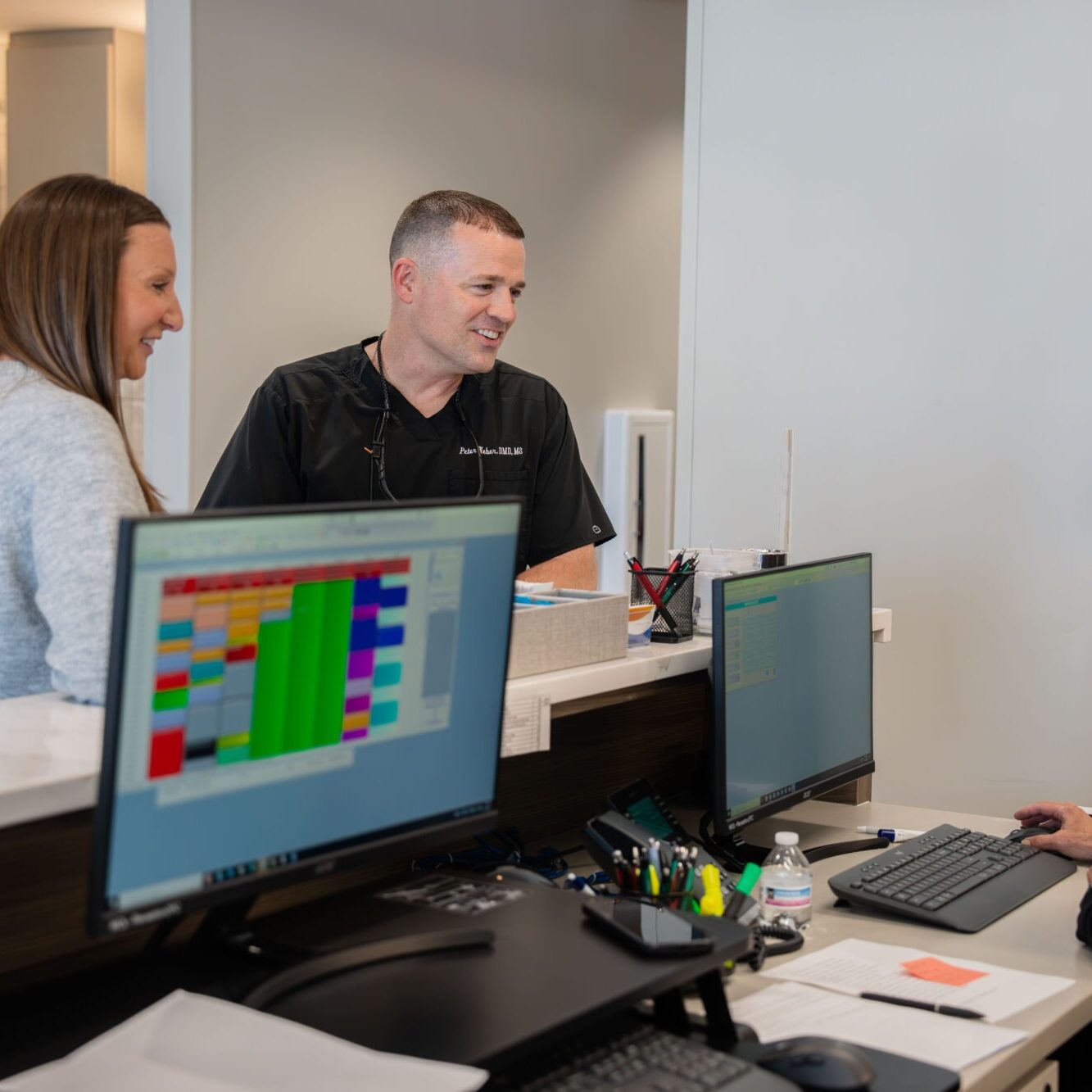 Patient consultation at Klein Walker & Weber Orthodontics with staff discussing treatment options, modern office setting, digital scheduling on computer screens.