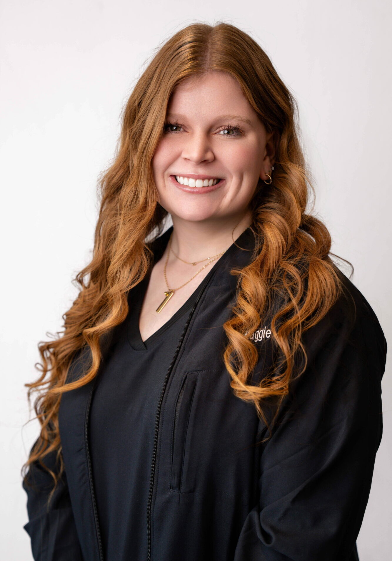 Evoto Maggie, orthodontic assistant at Klein Walker & Weber Orthodontics, smiling with long curly hair, wearing a black uniform, set against a neutral background.